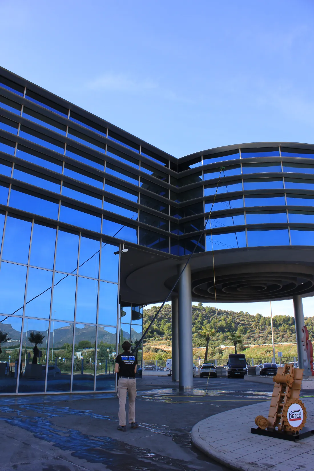 Operario de Brillaval limpiando con pértiga la fachada curva de cristal del edificio de Blumaq.