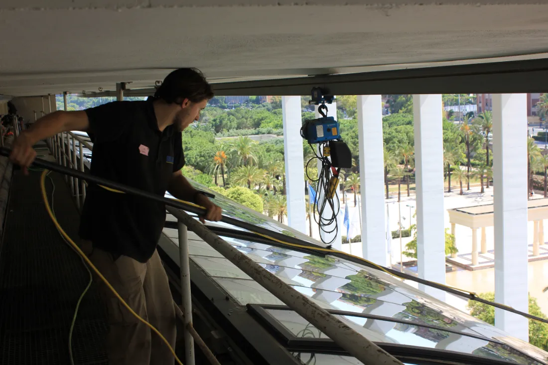 Operario de Brillaval limpiando la cubierta acristalada del Palau de la Música, con los jardines del Turia al fondo.